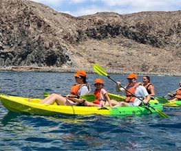 familia haciendo kayak en el mar con montaña de fondo