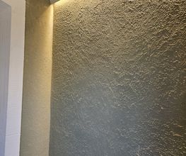 Exklusive Akzentwand mit Licht: Strukturierte, dunkle Wandfläche, die durch eine warme LED-Voutenbeleuchtung perfekt in Szene gesetzt wird.