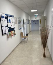 Flurbereich mit Pinnwand und Plakaten an der Wand. Mehrere Türen zu Räumlichkeiten. Ein dekorativer Strauch aus Zweigen und ein Stuhl.