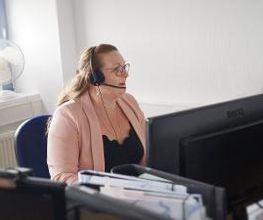 Teilnehmerin sitzt am Arbeitsplatz und kommuniziert mit den anderen Teilnehmenden und Dozent:innen über Headset.