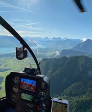 A spectacular view captured during a FunFlights scenic helicopter tour! From inside the cockpit, with the rotor blade in sight, guests can admire the impressive Stockhorn mountain rising above lush green forests, the turquoise-blue Lake Thun shimmering be
