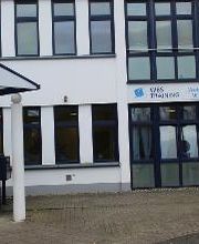 Außenansicht des Schulungsgebäudes in kooperativer Nachbarschaft mit dem privaten Berufskolleg. Weiße Fasade mit WBS TRAINING Schriftzug und Logo.