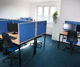 Dieses Bild zeigt einen Schulungsraum. Zu sehen sind Schreibtische, welche jeweils mit zwei Bildschirmen, einer Tastatur, Maus und Headset ausgestattet sind.