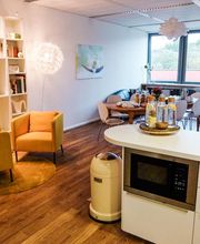 Aufenthaltsraum mit Sitzecke, Bücherregal und Tisch.