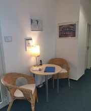 Eine kleine Sitzecke bestehend aus 2 gemütlichen Stühlen, einem Tisch und einer kleinen Lampe. Auf dem Tisch liegt Informationsmaterial und an der Wand hängen einige Bilder.