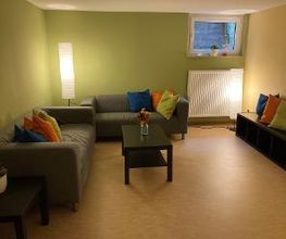 Pausenraum mit zwei Sofas und bunten Kissen sowie einem Tisch und Sitzbank. 2 Stehlampen sorgen für eine entspannte Atmosphäre.