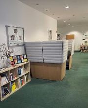 Eingangsbereich mit Sitzbereich. Links ein Bücherregal, rechts ein Hängesessel. Im Hintergrund ein weiteres Regal und Plakate.