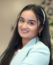 Portrait einer Mitarbeiterin mit langen schwarzen Haaren, die freundlich in die Kamera lächelt.