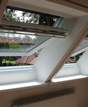 Ein moderner Raum mit zwei geöffneten Velux-Dachfenstern, die eine klare Aussicht auf grüne Bäume bieten und viel Tageslicht hereinlassen.