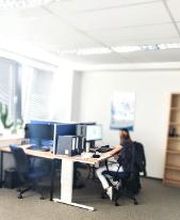 Teilnehmerraum mit Teilnehmerin am Arbeitsplatz lernend mit Regal im Hintergrund und Ventilator