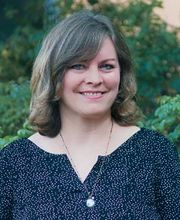 Eine Frau mit mittellangen dunkelblonen Haaren und gepunkteter Bluse.