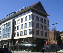 Ein vierstöckiges weißes Gebäude mit Spitzdach an einer Straßenkreuzung.