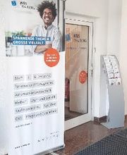 Eingangstür und Werbeaufsteller WBS TRAINING, rechts ein Flyerständer.