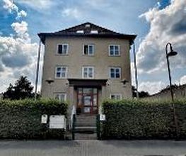Gelbes Gebäude mit grüner Hecke und Treppen zum Eingang