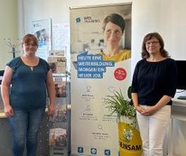 2 Frauen stehen neben einem WBS TRAINING Roll Up Banner und schauen freundlich.