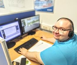 Teilnehmer schaut strahlend in die Kamera und arbeitet am PC und freut sich das sein Kurs gut läuft