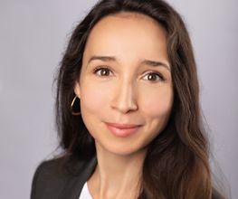 Portrait einer Mitarbeiterin mit braunen Haaren und Augen, die sympathisch in die Kamera schaut.