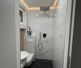Komplette Badsanierung aus einer Hand mit bodengleicher Dusche, großformatigen Fliesen und individuell gestalteter Decke mit direkter und indirekter Beleuchtung.