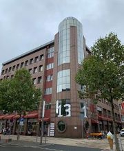 Außenansicht vom Gebäude an einer Straße. Hellbraune Fassade mit vielen Fenstern.