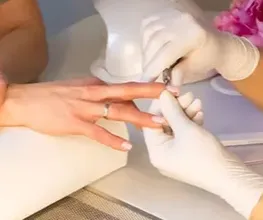 Das Bild zeigt eine professionelle Maniküre, bei der die rechte Hand einer Frau gepflegt und kosmetisch behandelt werden. Die Hand liegt stabil auf einer sauberen Unterlage, während eine Fachkraft die Nägel formt, vorbereitet oder pflegt. Die Szene wirkt ruhig, hygienisch und präzise. Der Fokus liegt auf den Händen der Kundin und den professionellen Handgriffen der Maniküre-Spezialistin, die typische Werkzeuge und Techniken für die Nagelbehandlung einsetzt.