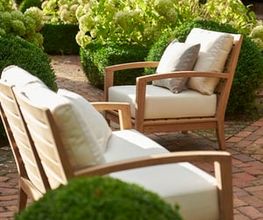 Zwei elegante Gartenstühle mit hellen Polstern stehen einladend inmitten eines gepflegten Gartens mit üppig blühenden Hortensien. Die harmonische Komposition strahlt Ruhe, Komfort und natürliche Schönheit aus.