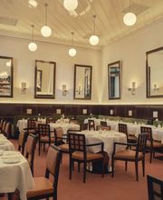 Classic dining room with round tables, white linens, and globe pendant lights.