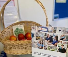 Bio-Obstkorb und Aufsteller mit Fotocollage von Teilnehmer:innen und Mitarbeiter:innen.