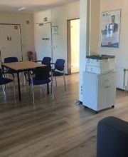 Pausenbereich für Teilnehmende mit einem Tisch und mehreren Stühlen und einem Drucker. Rechts befinden sich mehrere Türen und Poster der WBS TRAINING.