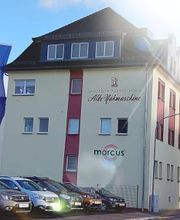 Mehrstöckiges Gebäude mit Firmenwerbung auf der Fassade. Davor stehen mehrere Autos.