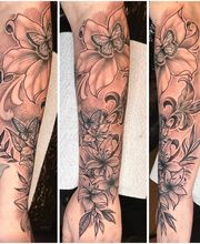 Filigranes Blackwork-Tattoo mit großen Blüten, Schmetterlingen, Blättern und Ornamenten als florales Unterarm-Motiv.