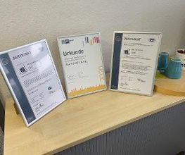 Regal mit 3 Urkunden. Daneben 2 blaue und eine weiße Tasse