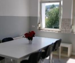 Ein großer weißer Tisch mit 6 Stühlen. Auf dem Tisch steht eine Vase mit Blumen.