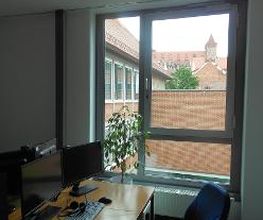 Ein Arbeitsplatz mit zwei Monitoren und einer Tastatur und Maus vor einem Fenster.