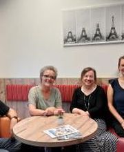 Ein Bild vom Team am Standort Leipzig Mitte. Die Personen sitzen auf einer Bank im Pausenraum und lächeln freundlich in die Kamera. Im Hintergrund hängt ein Bild vom Eifelturm in Paris.