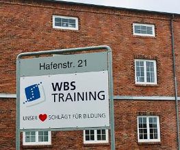 Ansicht des Außengebäudes, roter Backsteinbau mit weißen Sprossenfenstern. Davor steht ein WBS TRAINING Schild.