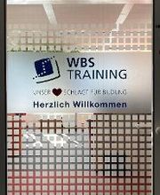 Glastür im Eingangsbereich. Schild mit Aufschrift „WBS TRAINING – Unser Herz schlägt für Bildung – Herzlich Willkommen“