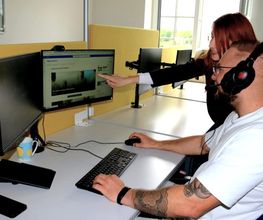 Eine Mitarbeiterin der WBS TRAINING zeigt einem Teilnehmenden, der im Schulungsraum an seinem Arbeitsplatz sitzt, etwas am PC/Bildschirm.