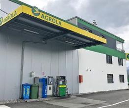 AGROLA Tankstelle in Oberbuchsiten; Eine Tanksäule mit Zahlterminal; daneben auch AdBlue Tanksäule; grüner Mülleimer und PET Behälter; überdacht; rechts weiss-grüne Hausfassade mit AGROLA Logo