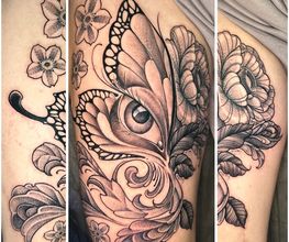 Detailreiches Black-and-Grey-Tattoo mit Schmetterling, Auge, Blüten, Blättern und ornamentalen Linien im femininen Fineline-Stil.