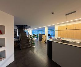 mediaService Bremen | Full-Stack Werbeagentur - Blick in das großzügige, offene Foyer einer Agentur mit dem Empfangstresen, einer dunklen Treppe in das Obergeschoss und angrenzenden Büroarbeitsplätzen.