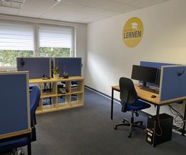 Mehrere Arbeitsplätze mit 2 Bildschirmen, einem Bürostuhl, Tastatur, Maus und Headset. Im Raum steht ein Regal mit Pflanzen.