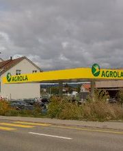 AGROLA Tankstelle in Rickenbach Sulz; diesige Aufnahme; vorne Strasse mit Fussgängerstreifen; links Totem mit AGROLA Logo und digitaler Preisanzeige; dahinter Wohnhäuser; rechts Tankstellendach