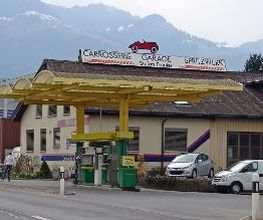 AGROLA Tankstelle in Benken. Geschwungene Glasüberdachung mit gelbem Metall. Zwei Tanksäulen. Im Hintergrund Gebäude mit Schild Carrosserie Garage Spritzwerk Schriftzug