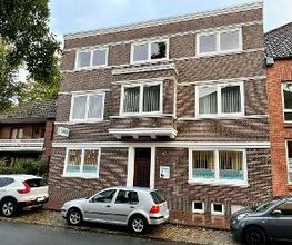 Ein Backsteinhaus mit drei Etagen. Davor sind 3 Autos geparkt