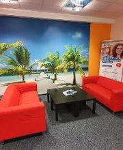 Pausenbereich bestehend aus 2 roten Sofas mit einem kleinen schwarzen Tisch. Großes Wandbild von einem Strand mit Palmen. 