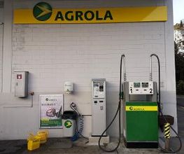 AGROLA Tankstelle in Ennetbürgen. Eine Tanksäule mit Tankautomat. Mülleimer und gelber Putzeimer und Giesskanne daneben. Über der Tanksäule AGROLA Banner mit Diskus.