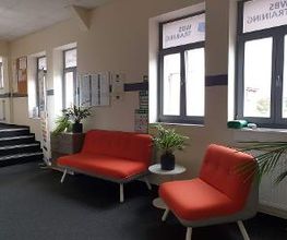 Wartebereich mit zwei roten Sofas und Grünpflanzen.