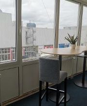 Sitzgelegenheit am Fenster bestehend aus einem modernen Hochtisch und 2 Stühlen. Auf dem Tisch steht eine Topfpflanze.