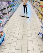 E&E Gebäudereinigung Gründliche Bodenreinigung in einem Supermarktgang, bei der eine Fachkraft mit Besen lose Verschmutzungen auf hellen Fliesen entfernt, um ein sauberes und gepflegtes Einkaufserlebnis zu gewährleisten.