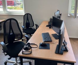 Moderner Arbeitsbereich ausgestattet mit 2 Bildschirmen, Tastatur, Maus und Headset sowie 2 schwarzen, komfortablen Bürostühlen. 